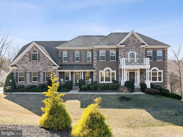 colonial home with stone siding, a balcony, and a front yard