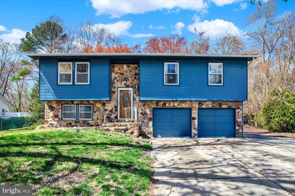 raised ranch with stone siding, a front yard, concrete driveway, and a garage