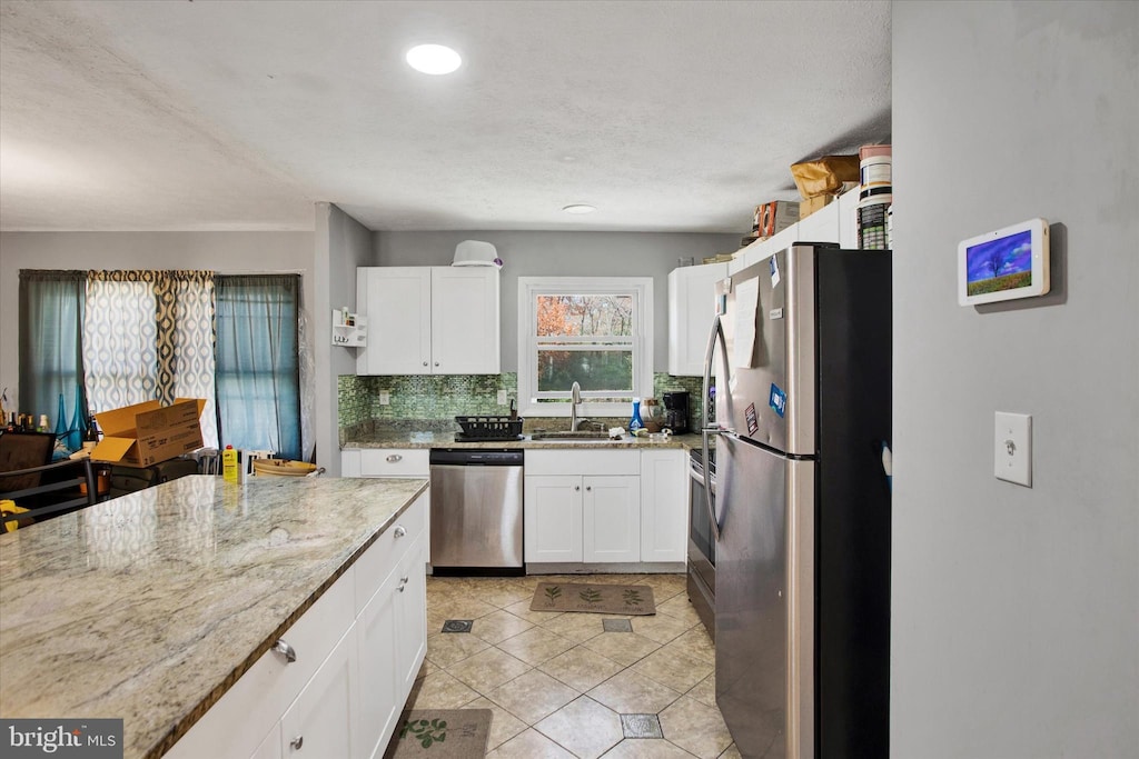 kitchen featuring light stone countertops, stainless steel appliances, white cabinetry, a sink, and backsplash