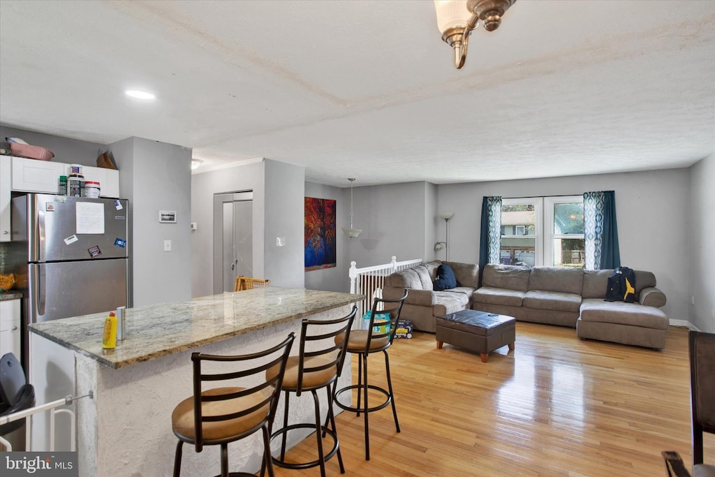 kitchen with white cabinetry, a breakfast bar, light wood-style floors, freestanding refrigerator, and light stone countertops