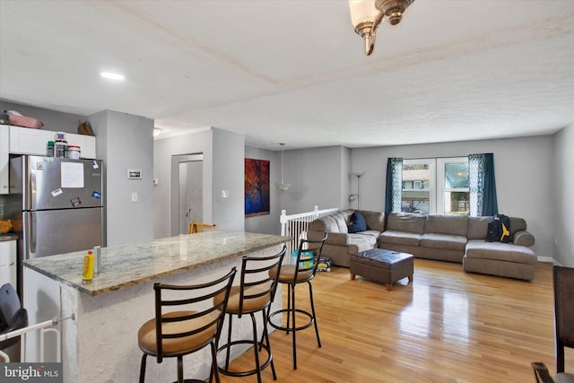 kitchen with white cabinetry, a breakfast bar, light wood-style floors, freestanding refrigerator, and light stone countertops