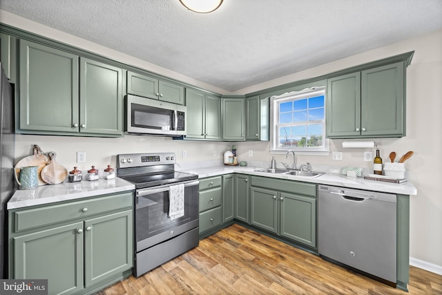 kitchen featuring green cabinets, a sink, appliances with stainless steel finishes, and light wood-type flooring