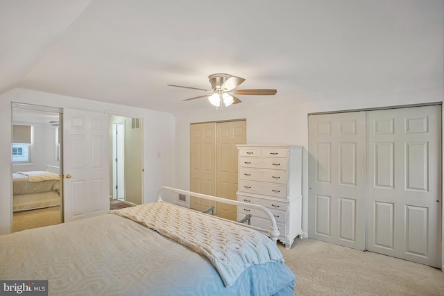 bedroom with light colored carpet, a ceiling fan, visible vents, lofted ceiling, and multiple closets
