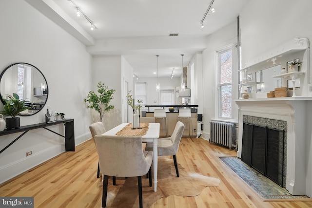 dining room featuring radiator, track lighting, light wood-type flooring, and a tiled fireplace
