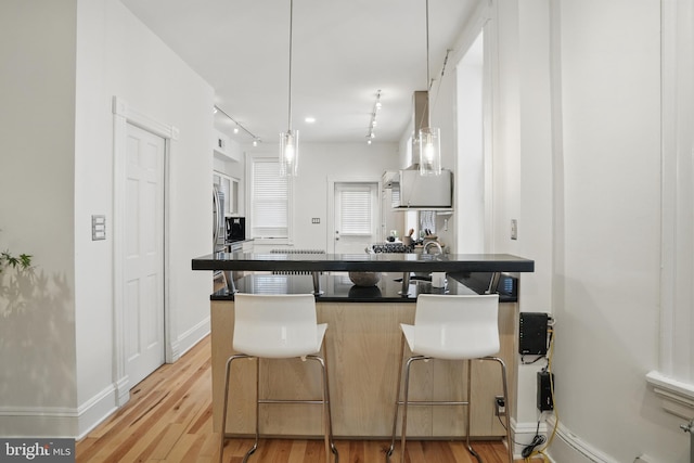 kitchen with dark countertops, light wood-type flooring, a breakfast bar, a peninsula, and baseboards