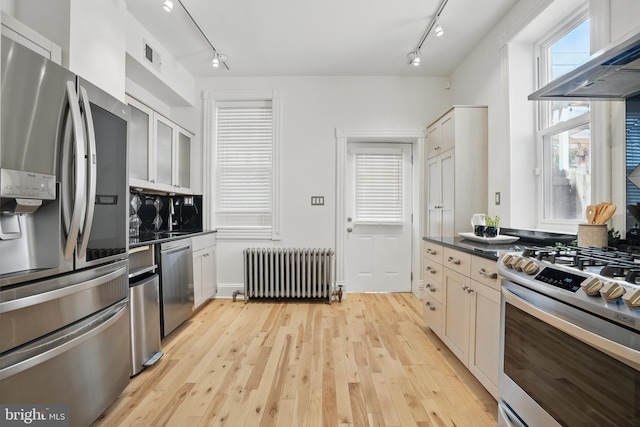 kitchen with stainless steel appliances, radiator heating unit, track lighting, and wall chimney exhaust hood