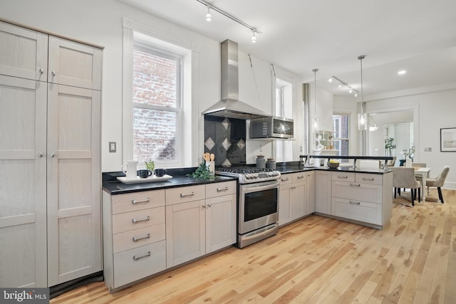 kitchen with stainless steel gas stove, track lighting, wall chimney range hood, and dark countertops
