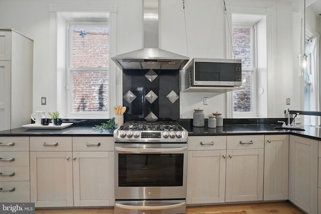 kitchen featuring stainless steel appliances, island range hood, dark countertops, backsplash, and a sink