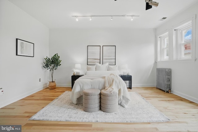 bedroom with radiator, wood finished floors, rail lighting, and baseboards