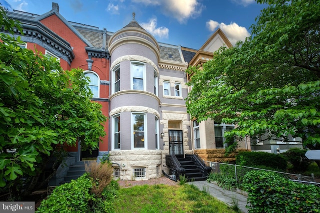 victorian house with fence, a high end roof, and brick siding