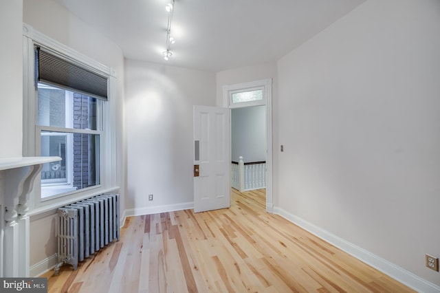 empty room with radiator heating unit, wood finished floors, baseboards, and rail lighting