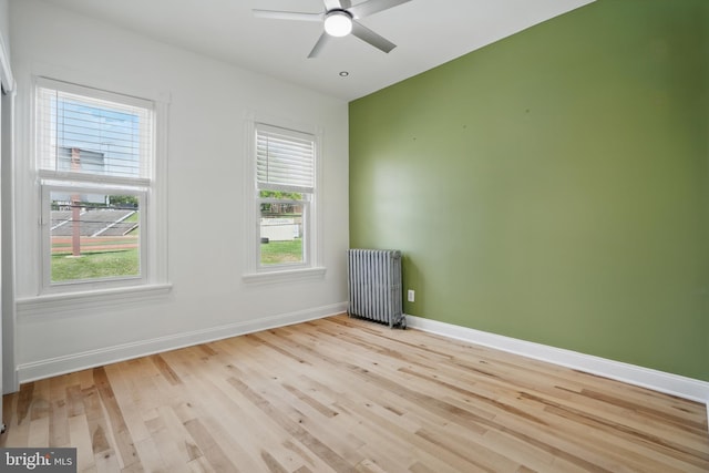 spare room featuring radiator heating unit, light wood finished floors, baseboards, and ceiling fan