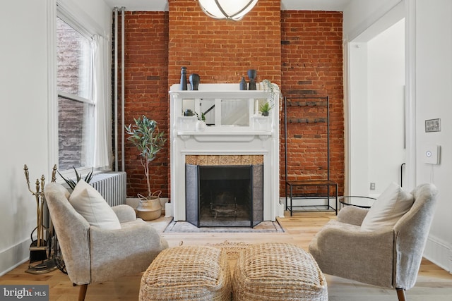 sitting room with brick wall, wood finished floors, a fireplace, and baseboards