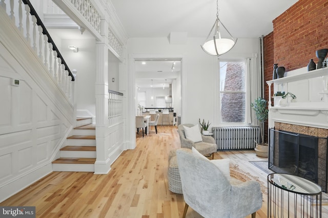 living room with radiator, stairs, light wood-style flooring, a fireplace, and brick wall