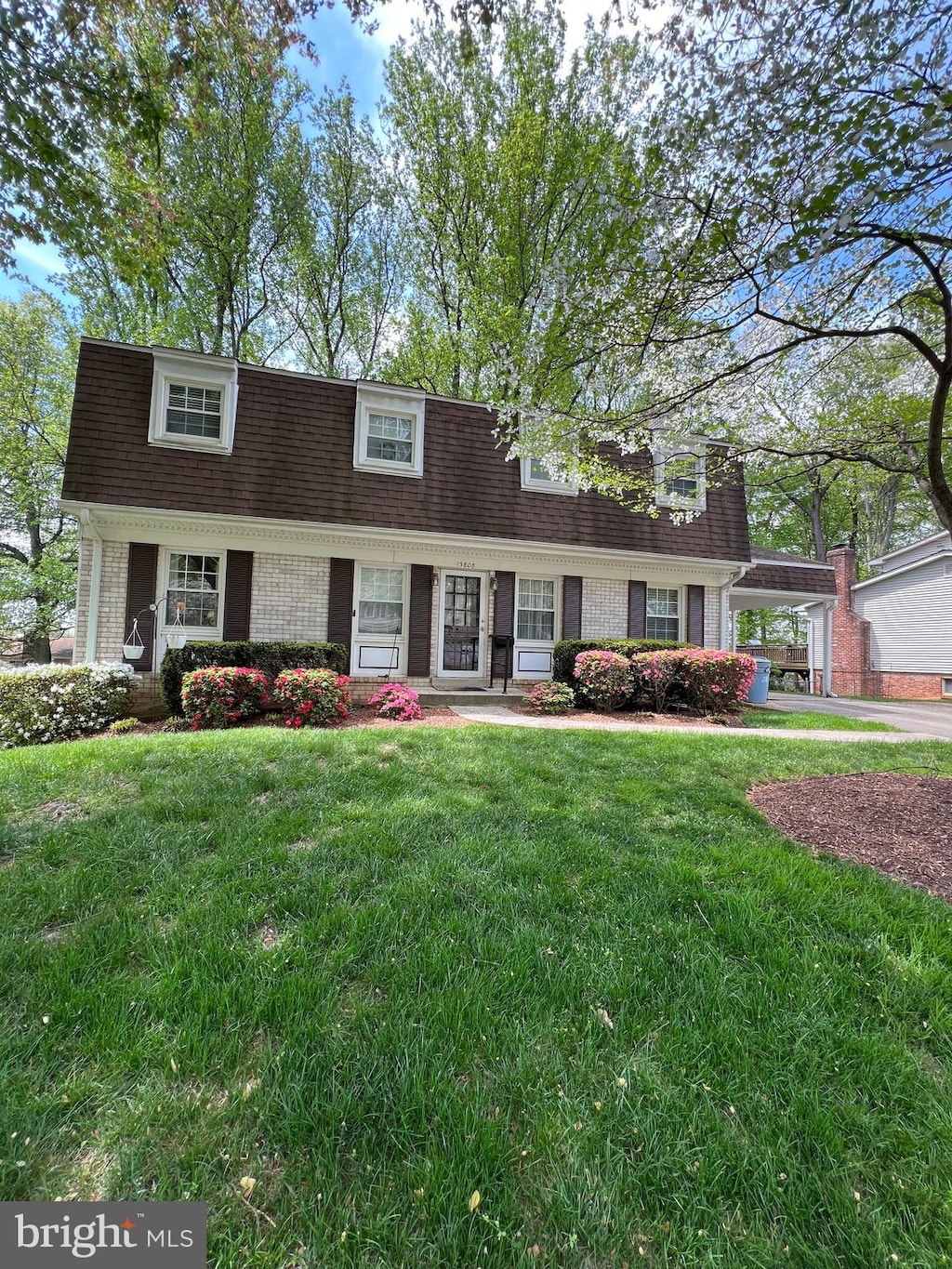 view of front of home featuring brick siding, a shingled roof, a front yard, and a carport