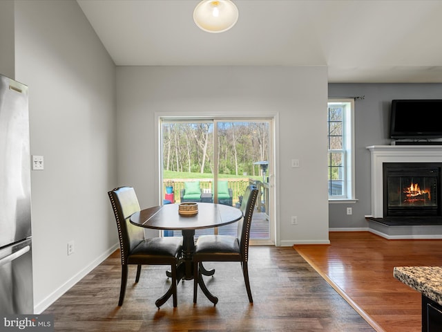 dining space with a glass covered fireplace, baseboards, and wood finished floors