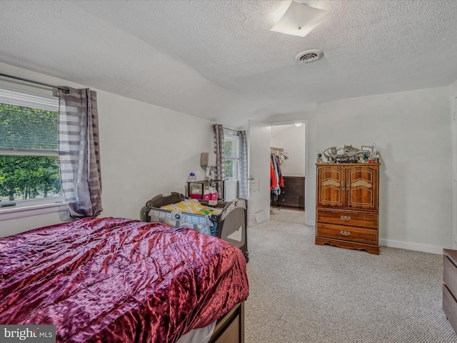 bedroom with a textured ceiling, visible vents, carpet, baseboards, and a spacious closet