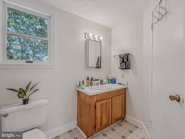 half bath with baseboards, toilet, vanity, and a textured ceiling