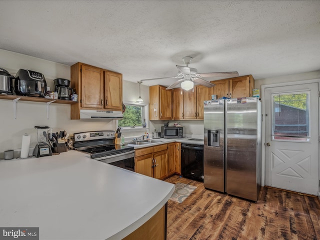 kitchen featuring light countertops, stainless steel appliances, under cabinet range hood, brown cabinetry, and wood finished floors