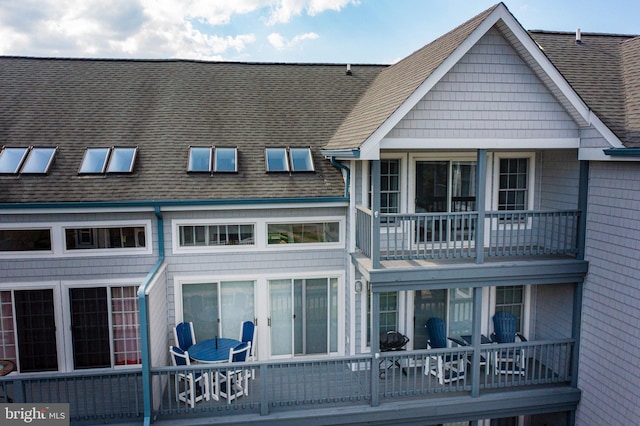 back of property featuring a balcony and a shingled roof