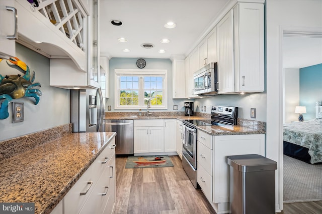 kitchen featuring white cabinetry, stainless steel appliances, a sink, light wood finished floors, and visible vents