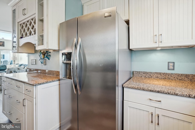 kitchen featuring glass insert cabinets, white cabinetry, light stone countertops, and stainless steel refrigerator with ice dispenser