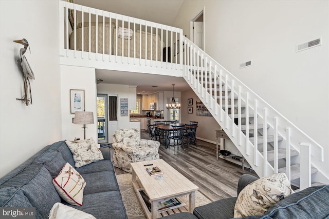 living room featuring wood finished floors, a towering ceiling, stairs, and visible vents