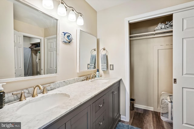 full bathroom with baseboards, double vanity, a sink, and wood finished floors