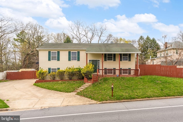 split foyer home with covered porch, fence, and a front lawn