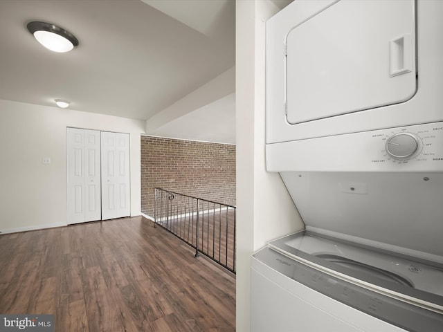 washroom with laundry area, wood finished floors, stacked washing maching and dryer, and brick wall