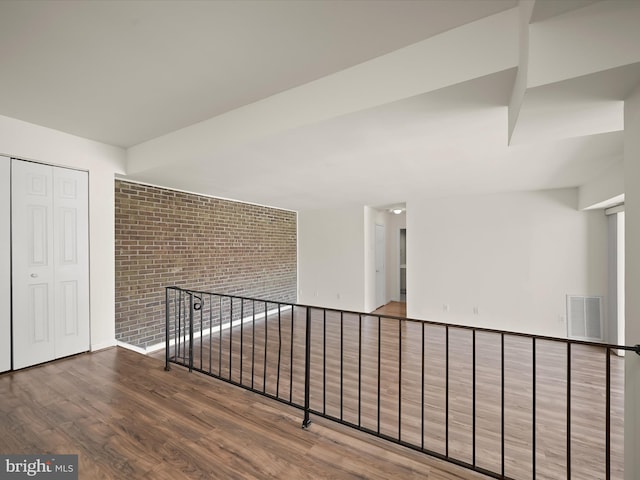 unfurnished room featuring visible vents, brick wall, and wood finished floors