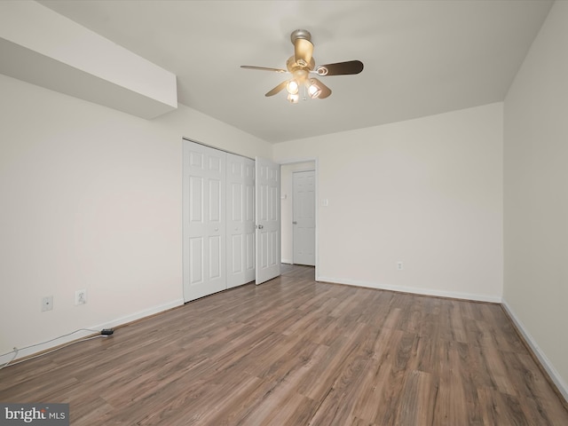 unfurnished bedroom with baseboards, a closet, wood finished floors, and ceiling fan