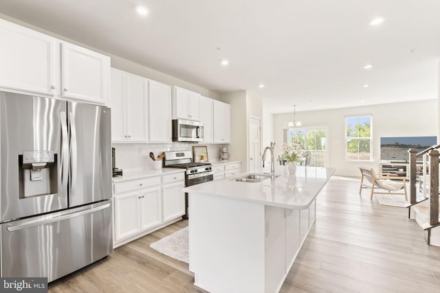 kitchen with a center island with sink, light wood-type flooring, white cabinetry, a sink, and stainless steel appliances