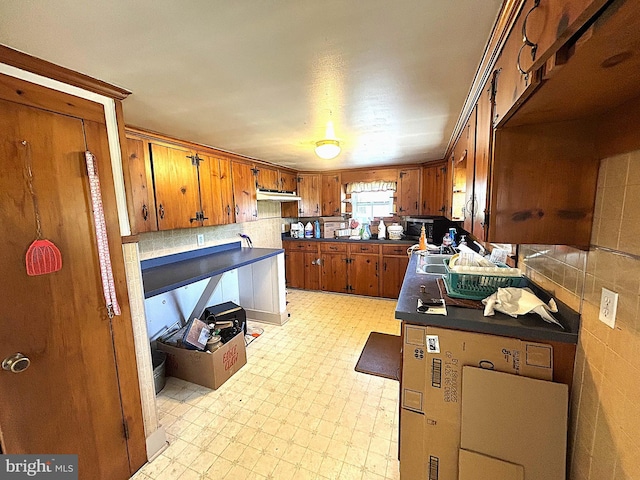 6637 Elton Dennis Rd, Willards, MD 21874 - kitchen featuring dark countertops, tasteful backsplash, brown cabinets, light floors, and under cabinet range hood