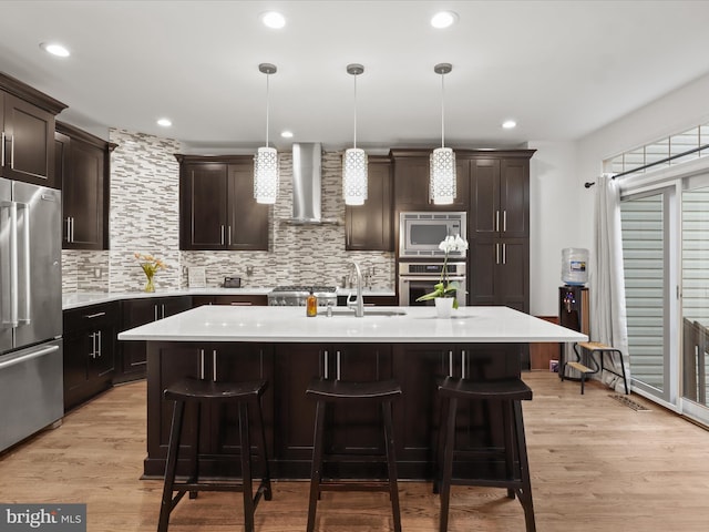 kitchen with decorative backsplash, light countertops, wall chimney exhaust hood, a sink, and appliances with stainless steel finishes