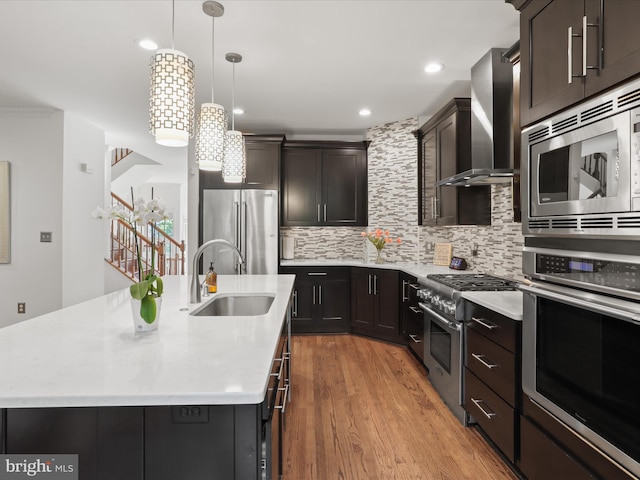 kitchen with a center island with sink, high quality appliances, light countertops, wall chimney exhaust hood, and a sink