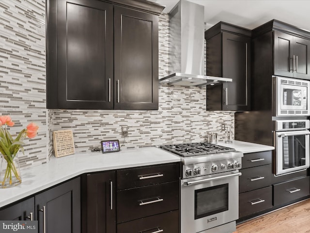 kitchen featuring wall chimney range hood, appliances with stainless steel finishes, light wood finished floors, light countertops, and tasteful backsplash