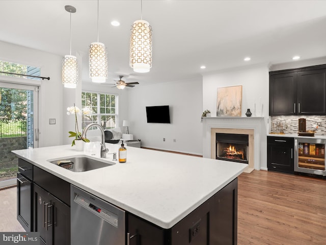 kitchen with stainless steel dishwasher, a ceiling fan, beverage cooler, a warm lit fireplace, and a sink