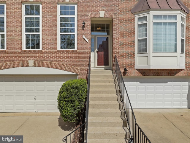 entrance to property with brick siding, an attached garage, and driveway