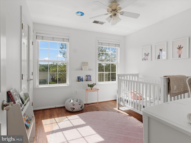 bedroom with a crib, multiple windows, wood finished floors, and visible vents