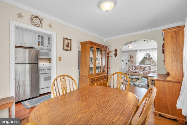 dining space featuring arched walkways, crown molding, and light wood-type flooring