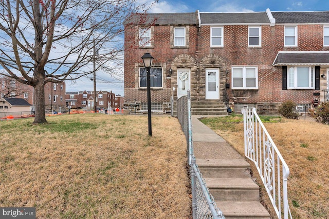 townhome / multi-family property featuring a front lawn, brick siding, and roof with shingles