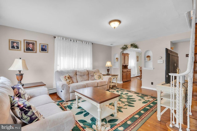 living area featuring a baseboard radiator, baseboard heating, light wood-style flooring, baseboards, and arched walkways