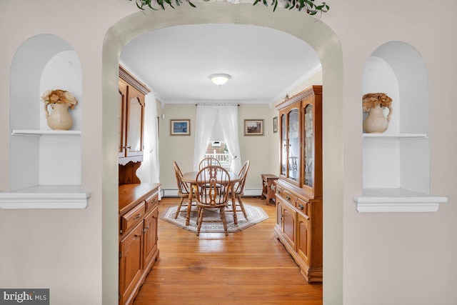 dining room featuring light wood finished floors, arched walkways, ornamental molding, and built in shelves