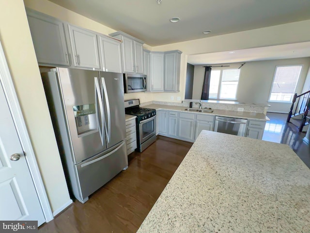 kitchen with stainless steel appliances, a sink, dark wood-style floors, a peninsula, and light stone countertops