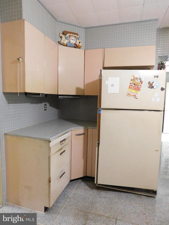 kitchen with light countertops, freestanding refrigerator, cream cabinetry, and decorative backsplash