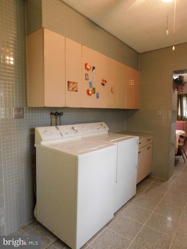 clothes washing area featuring washing machine and clothes dryer, cabinet space, and tile walls
