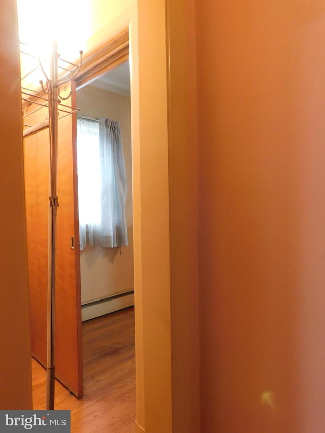 corridor with a baseboard heating unit and wood finished floors