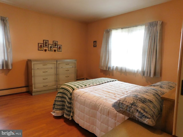 bedroom with a baseboard heating unit and wood finished floors