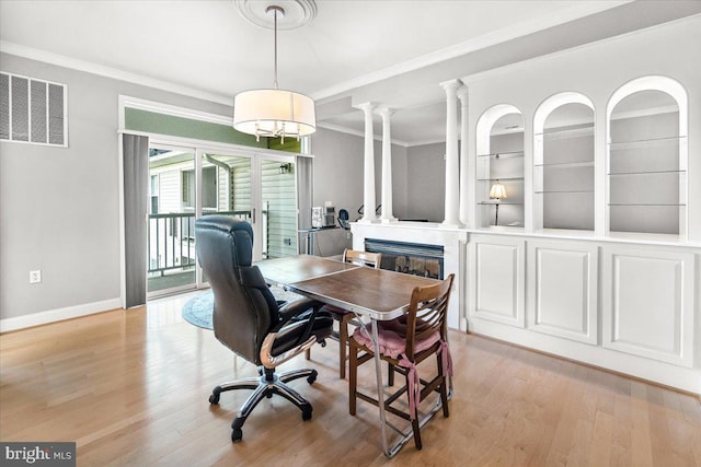 dining space with crown molding, visible vents, a glass covered fireplace, and light wood-type flooring